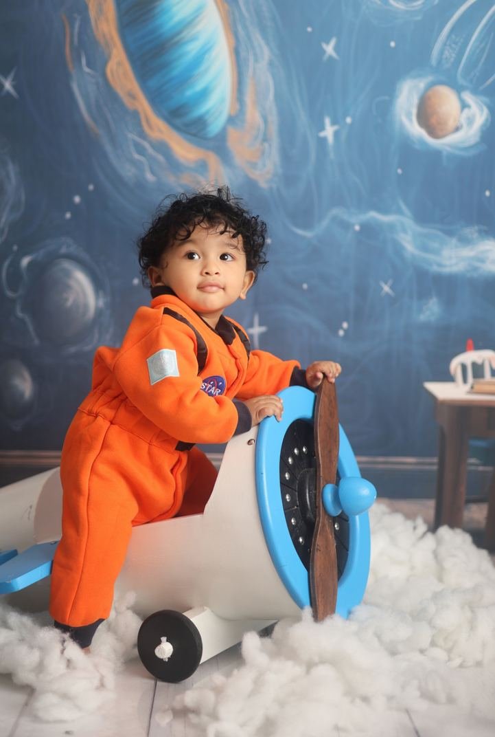 Baby in an orange astronaut suit beside a toy plane