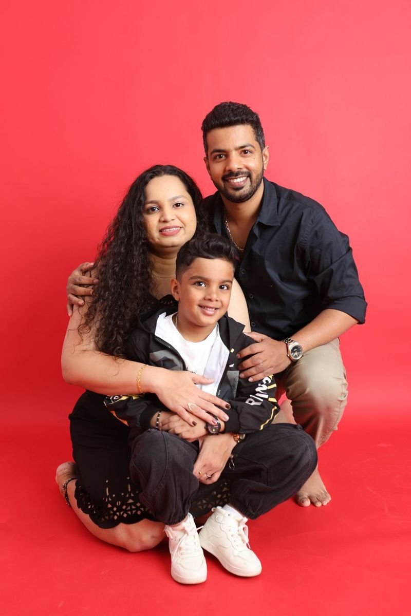 Family of three smiling on a red studio backdrop