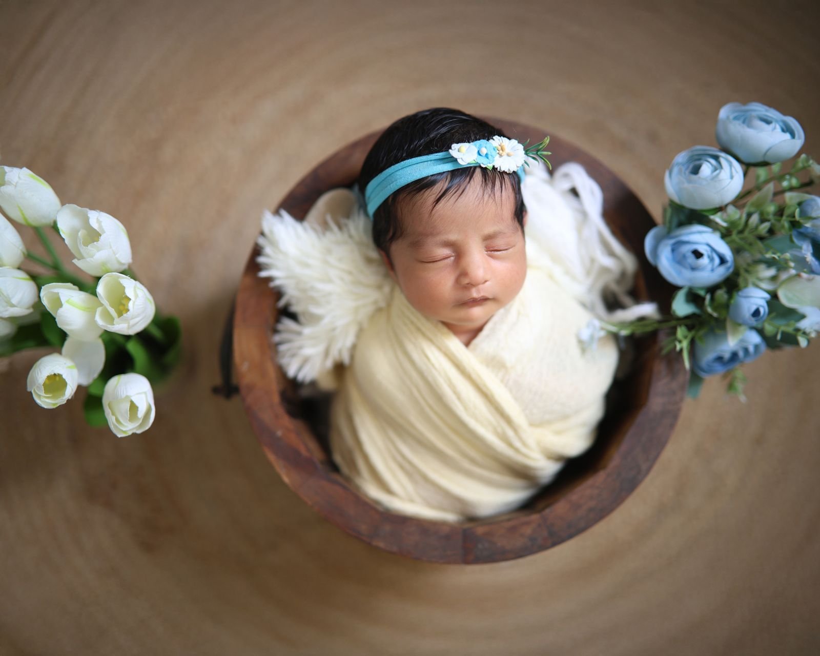 Newborn in a wooden bowl with flowers