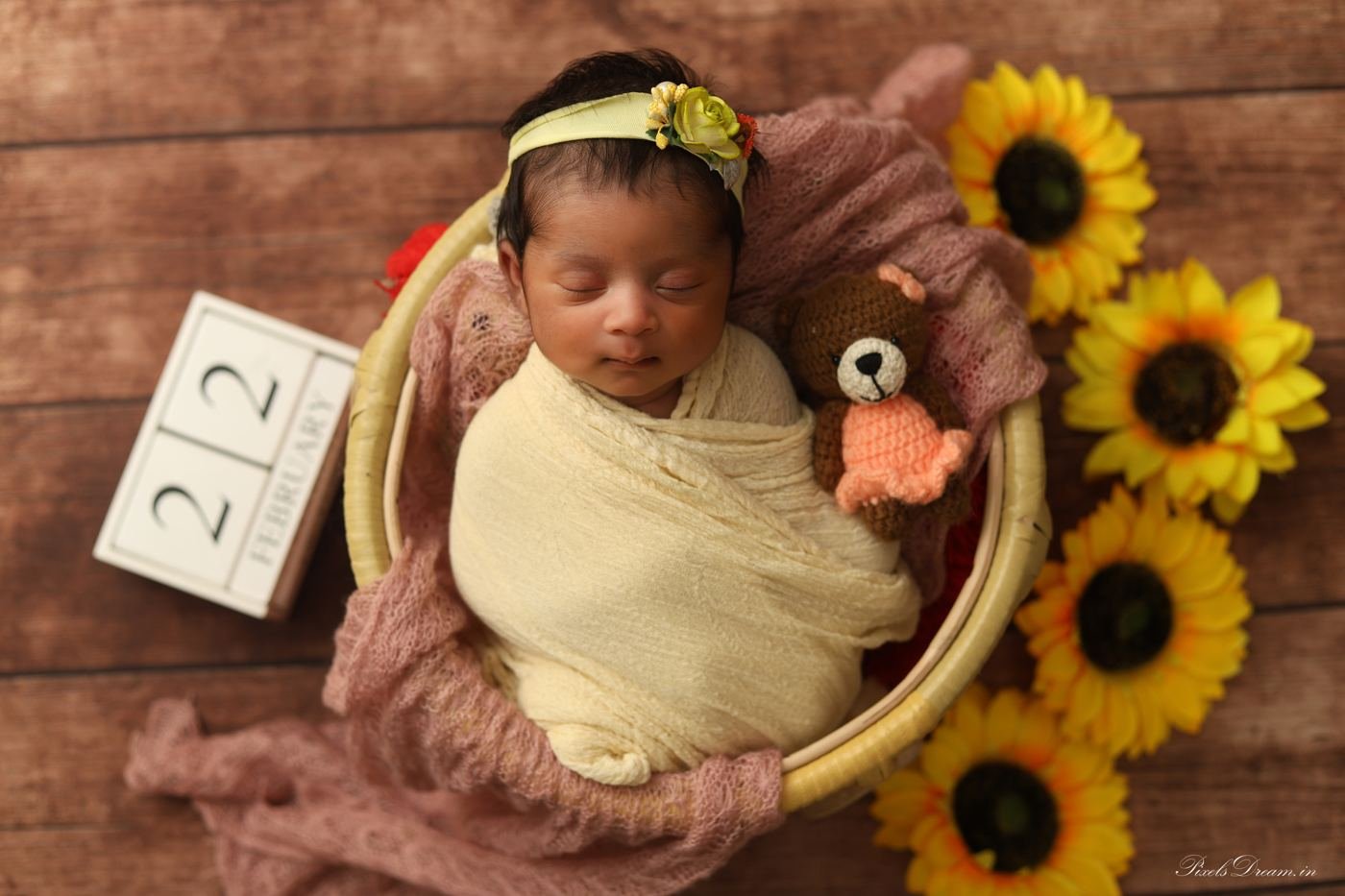 Newborn wrapped in yellow in a wooden tub with sunflowers